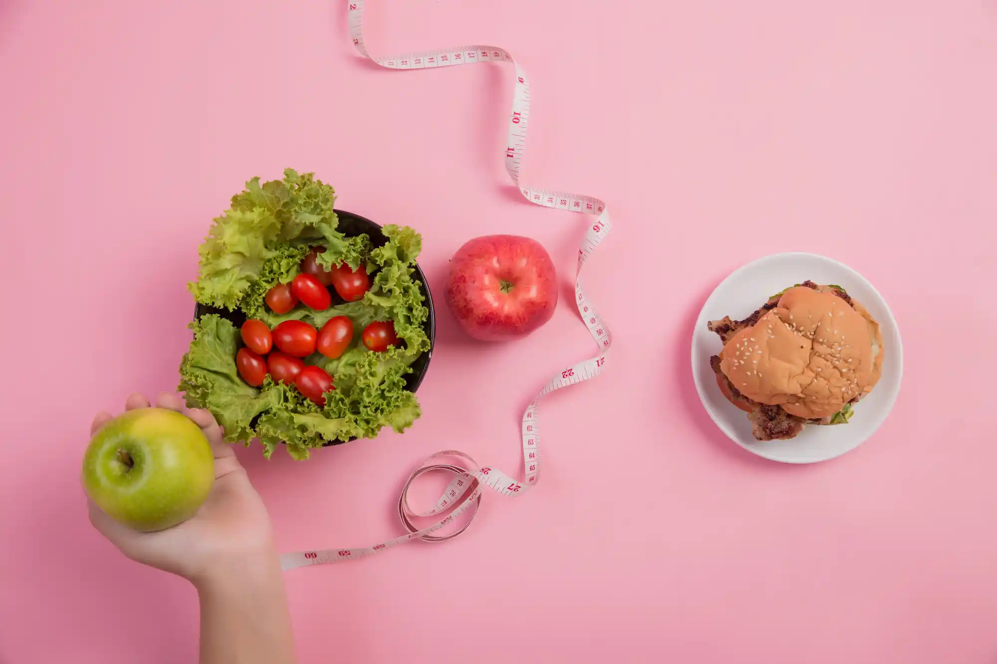 A hand holding a green apple versus a plate with a burger, with a measuring tape in the background, symbolizing nutritional choices