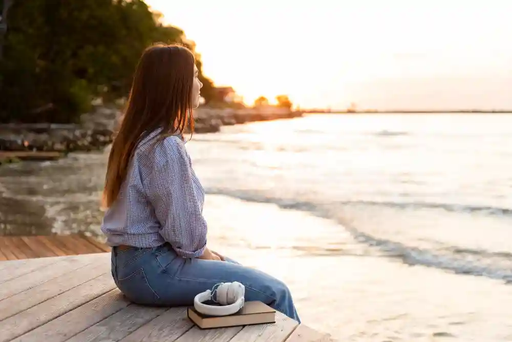 Woman sitting by the water looking at the sunset, illustrating mindful observation