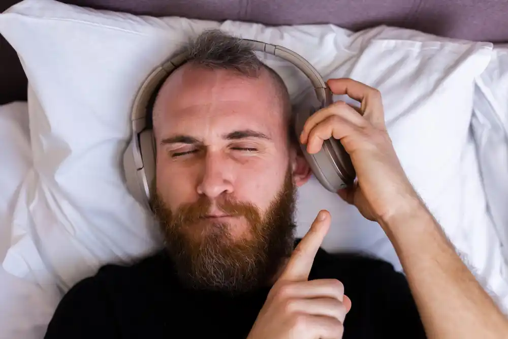 A man lying in bed with headphones, illustrating the potential risks of improper volume levels during sleep