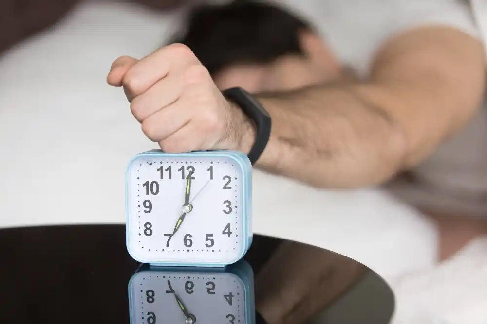 A person smashing an alarm clock in the morning, representing the frustration of waking up early