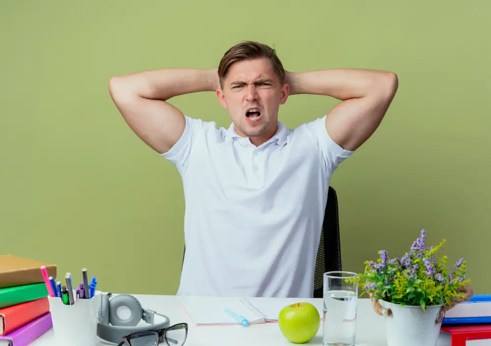 Frustrated man at desk pulling his hair, screaming, surrounded by work, representing workplace stress